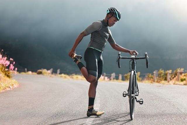 Fietser rekt zijn been naast een racefiets op een landweg